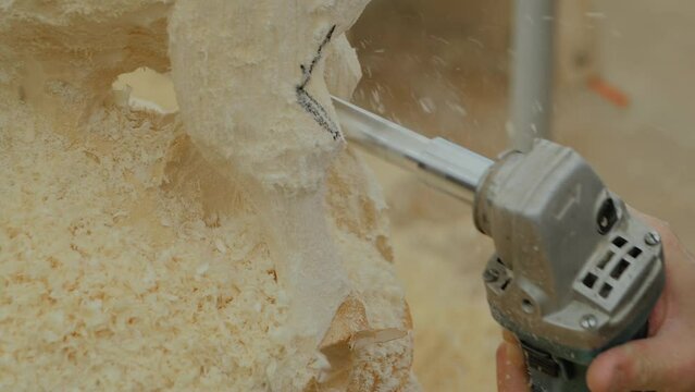 Close up: wood sculptor, carpenter using angle grinder with holes cutter saw attachment for carving wooden sculpture of goat - shavings flying in slow motion. Art, carpentry and hobby concept