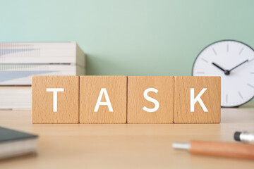 「TASK」と書かれた積み木、ペン、ノート、本、置き時計