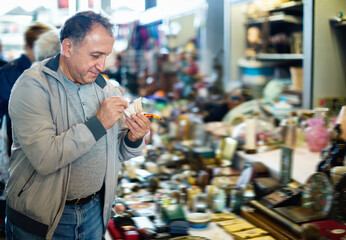 Positive smiling elderly man choosing interesting souvenirs at traditional flea market
