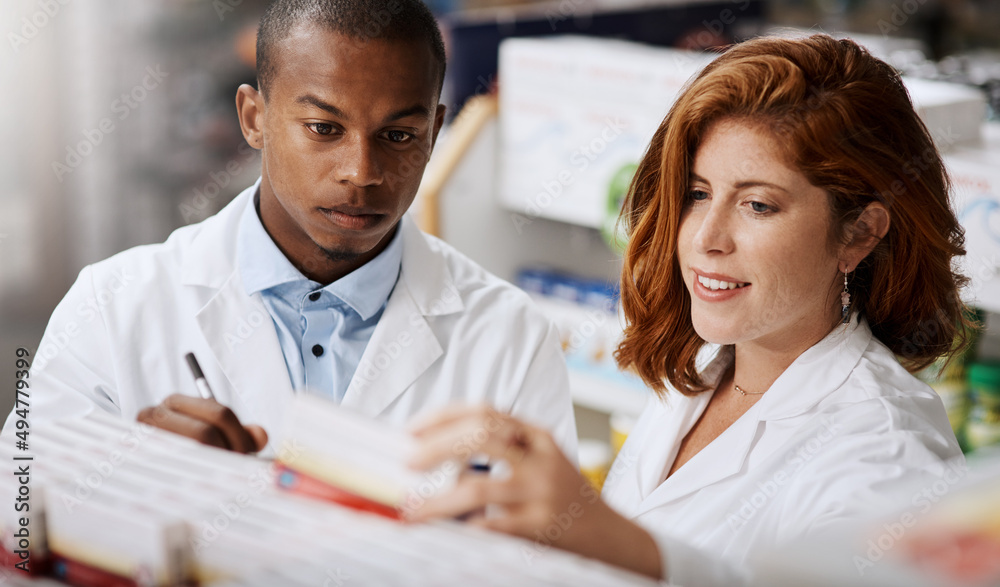 Poster updating all stock on their shelves. shot of two pharmacists working together in a chemist.