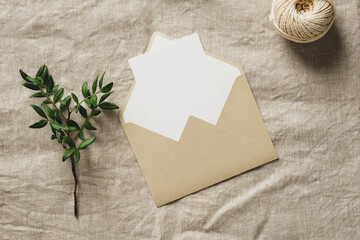 Beige paper envelope with blank card, green branch, twine rope on linen tablecloth. Wedding...