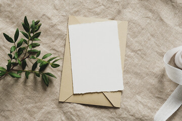 Blank paper card mockup, envelope, green branch, silk ribbon on linen tablecloth. Wedding...