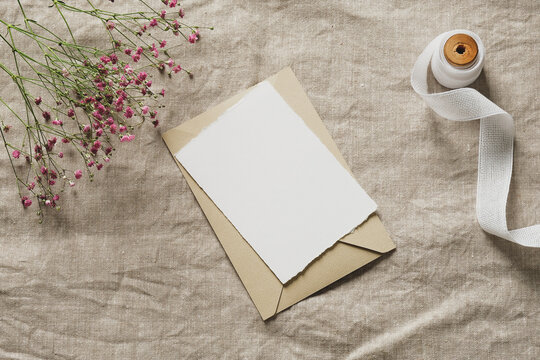 Wedding Invitation Mockup With Beige Envelope, Ribbon, Gypsophila Flowers On Linen Tablecloth. Wedding Stationery Set.