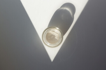 Concept of minimalist skincare routine. Top down view of a moisturizer jar with contrasting shadows.