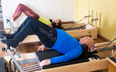 Older man doing exercises of remedial gymnastic on Pilates reformer in rehab clinic. Physical...