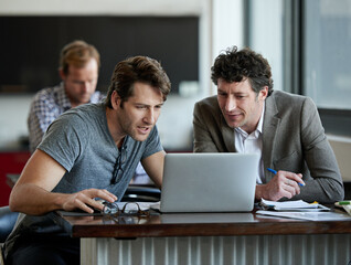 This is very interesting. Shot of two male colleagues talking together over a laptop.