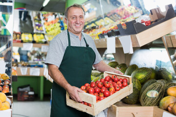 Smiling man employee showing box with natural tomatos in the hypermarket..