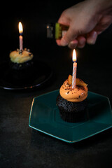 Chocolate Birthday cupcake with a single candle light on dark background.