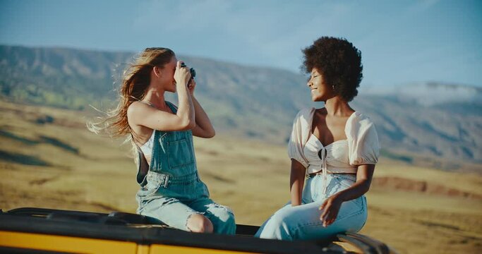 Two young women laughing and taking photographs on summer road trip, travel and adventure lifestyle