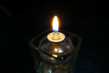 Liquid candle in glass holder with bright flame isolated on dark black background. Copy space.