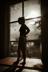 Fototapeta na wymiar Silhouette of a woman standing in the gym at sunset. woman has her hands on her hips