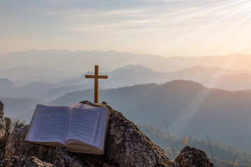 crucifix symbol and bible on top mountain with bright sunbeam on the colorful sky background - obrazy, fototapety, plakaty