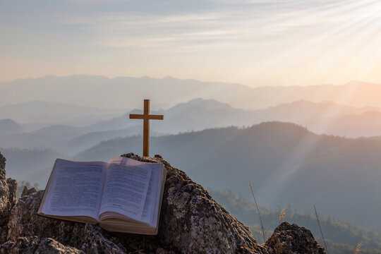 crucifix symbol and bible on top mountain with bright sunbeam on the colorful sky background