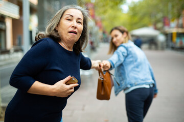 Street thief trying to steal handbag of scared elderly woman walking through city on warm autumn day