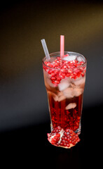 Fresh pomegranate juice with ice and fruit seeds on a black background.