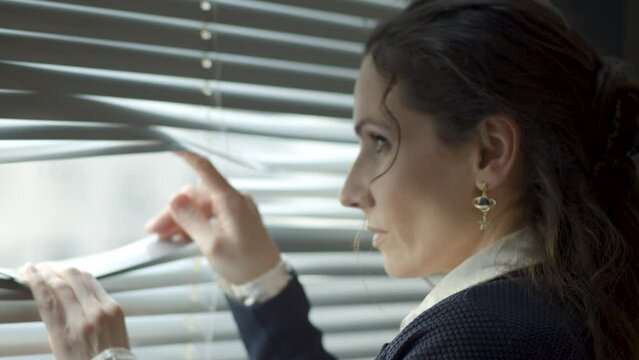 Strict business woman looking through window blinders and turning her head to something offscreen