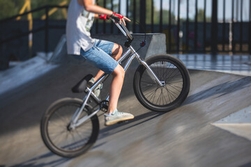 Skate park view with kids on a kick scooter doing tricks and stunts, boys in a skate park riding bmx bike and skate, playing and enjoying summer on new ramp, teenagers skateboarders and bmx riders