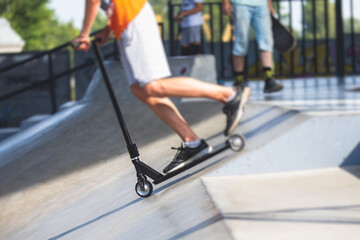 Skate park view with kids on a kick scooter doing tricks and stunts, boys in a skate park riding bmx bike and skate, playing and enjoying summer on new ramp, teenagers skateboarders and bmx riders