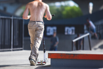 Skate park view with kids on a kick scooter doing tricks and stunts, boys in a skate park riding bmx bike and skate, playing and enjoying summer on new ramp, teenagers skateboarders and bmx riders