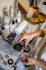 Closeup female hands putting luxury cosmetic into acrylic box with drawer storage organization