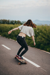 Back view, female skateboarder riding long board on the bike path , Green meadow in the background
