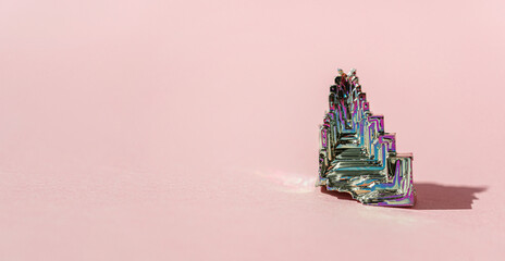 Synthetic bismuth Bismuthumcrystal with iridescent oxide film on pink background close up isolated....