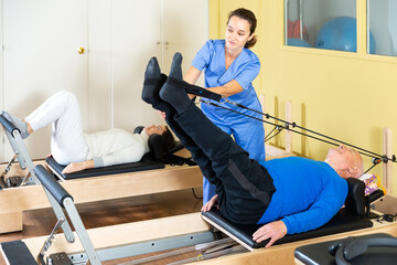 Professional female rehabilitation physician controlling movements of senior man doing exercises on...