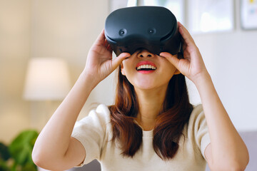 Young Asian woman feeling excited while using 360 VR headset for virtual reality/ metaverse at home