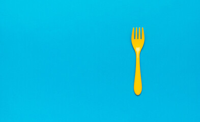 Beautiful plastic yellow fork on a blue background. Space for text. Flat lay.