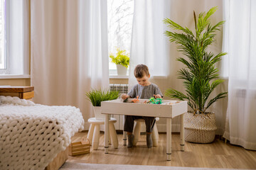 Cute male kid playing sensory box dinosaur world at comfortable home living room