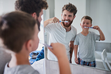 Start good oral habits early. Shot of a father and his little son brushing their teeth together in the bathroom at home.