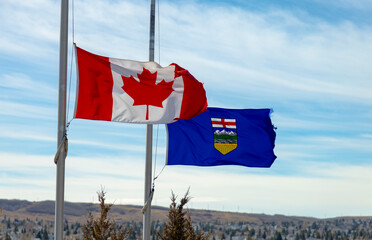 A Canadian flag and a province of Alberta Flag waving with the wind half-mast or half-staff refers to a flag flying below the summit a symbol of respect, mourning, distress, or in some cases, a salute - obrazy, fototapety, plakaty