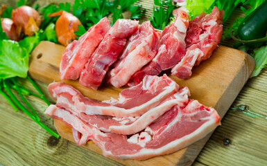 Raw lamb cutlets on wooden cutting board with parsley and vegetables