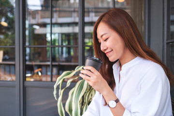Fototapeta premium Portrait image of a beautiful young asian woman holding and drinking hot coffee in paper cup