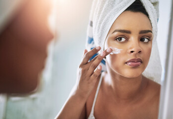 Hydrate your skin with good quality products. Shot of an attractive young woman applying moisturizer to her face in the bathroom.