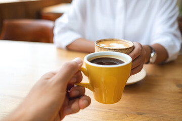Closeup image of a young couple people clinking coffee cups together in cafe