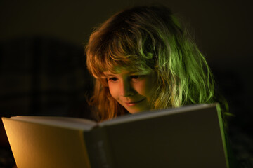 Boy reading bedtime story, dark room photo. Child reading a magic book in bed. Kid boy read books...