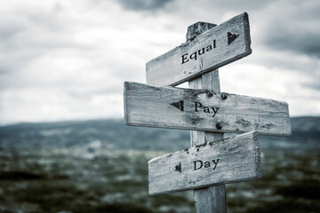 equal pay day text quote written in wooden signpost outdoors in nature. Moody theme feeling.