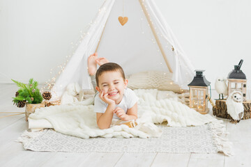 Little caucasian boy laughing while lying in a toy kids teepee in a white scandinavian christmas...