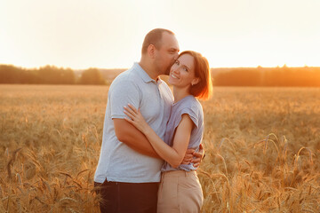 A man and a woman embrace against the background of the setting sun in a wheat field. Lovers at sunset in summer in nature.