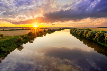 Fototapeta na wymiar Amazing view at scenic landscape on a beautiful river and colorful sunset with reflection on water surface and glow on a background, spring season landscape