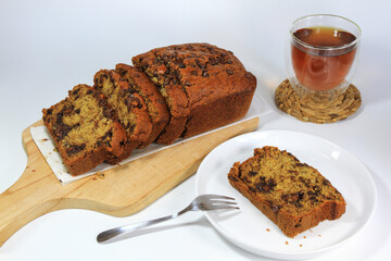 Sliced banana bread loaf on wooden board, a slice of banana bread on a plate, and a glass of tea. Breakfast menu.