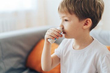 Little boy uses hormonal nasal spray while sitting on the couch.