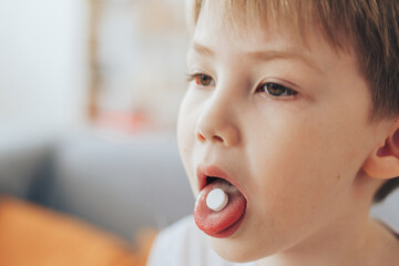 Little boy holds white round pill on his tongue.