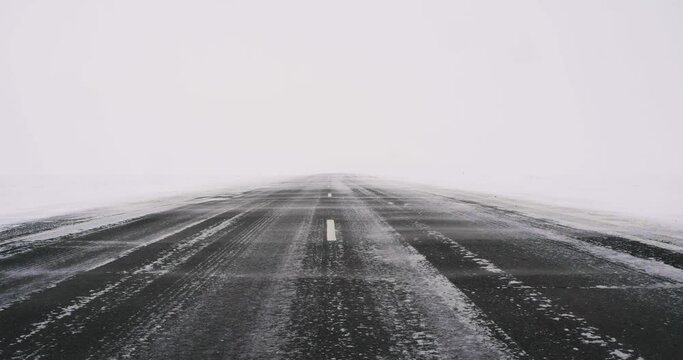 Snowstorm on the background of the road in the endless icy desert. Travel in extreme weather conditions.