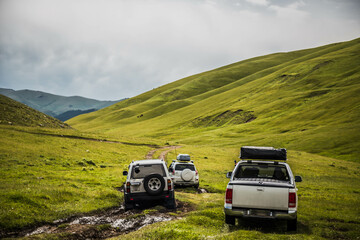 cars is moving along a dirt road. travel by car in the mountains. rough road in the steppe. jeeps make their way through the desert - obrazy, fototapety, plakaty