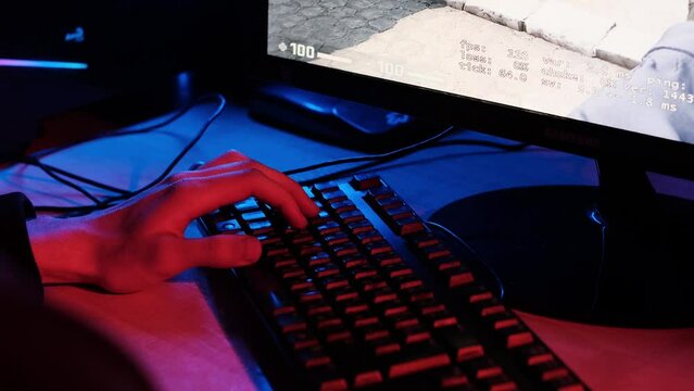 Hand playing on keyboard. Professional cyber video gamer studio room with personal computer, keyboard  in neon color background.