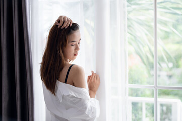 Sexy Asian woman opening the curtain after waking up in the morning