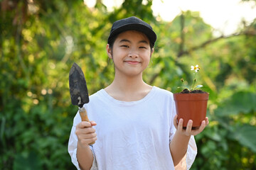 Smiling asian girl holding garden shovel and flower pot in hands. Concept of saving the world,...