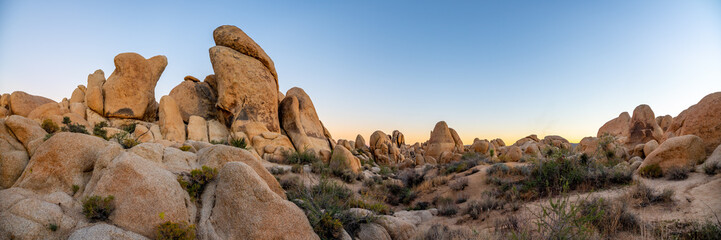 Joshua Tree National Park at sunset with large rock boulders in view and sun dipping below the...